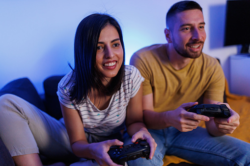 Young couple sitting on a couch in the living room and playing video games at night