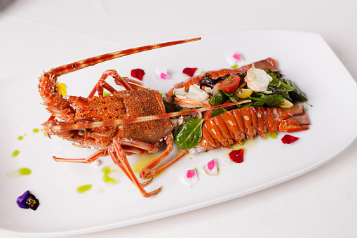 Lobster serving on a rectangular plate in fine dining, cut in half and filled with vegetables and baby spinach