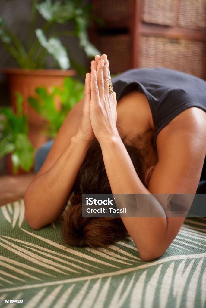 Woman practicing mediation and praying indoors. Zen,  spiritual person with head bowed down on a mat while holding hands in prayer inside her home. Female doing yoga exercise for peaceful lifestyle Finger Stock Photo