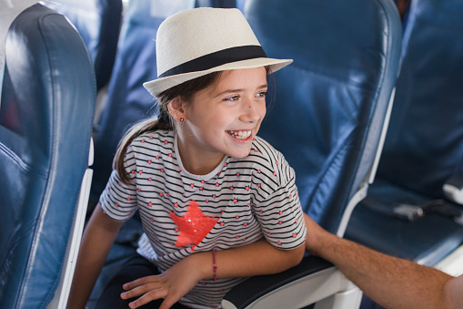 Cheerful young girl with toothy smile sitting on a plane with a summer hat on