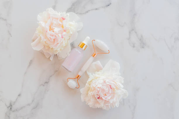 istock Face massage roller with natural essential oil in pipette bottle on marble background with peonies. Flat lay, top view. Facial skin care, body treatment concept. 1411604045