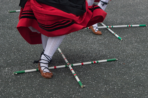 A Basque dancer in a traditional red and black costume performs the stick dance