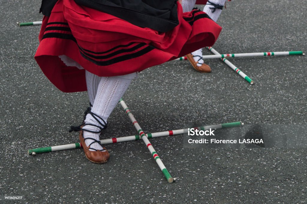 Basque dance in traditional costume with cross sticks on the floor A Basque dancer in a traditional red and black costume performs the stick dance Basque People Stock Photo