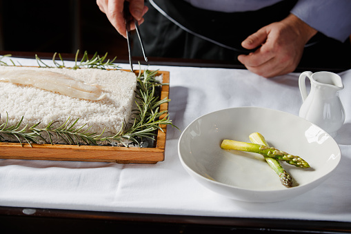Chef's hand holding tongs to pick up fish fillet grilled on hot Himalayan salt block in fine dining