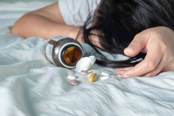 Asian woman in white shirt is lying unconscious on a white bed after overdosing on weight loss pills stock photo