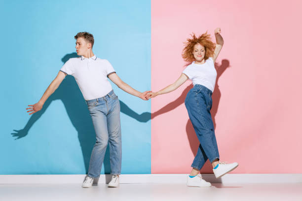 Portrait of young couple holding hands, dancing boogie woogie isolated over pink blue studio background Portrait of young couple holding hands, dancing boogie woogie isolated over pink blue studio background. Concept of youth, emotions, facial expression, love, relationship. Poster, ad boogie woogie dancing stock pictures, royalty-free photos & images