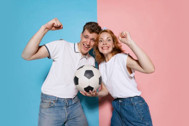 portrait of young couple, emotive football fans celebrating winning game isolated over pink blue studio background - club soccer fotos imagens e fotografias de stock