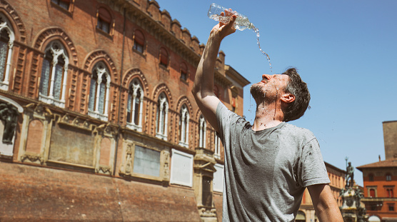 Mid-adult man standing in the Piazza del Nettuno or Piazza Maggiore by the Pallzzo d'Accursio and pouring cold water on his face to cool down.