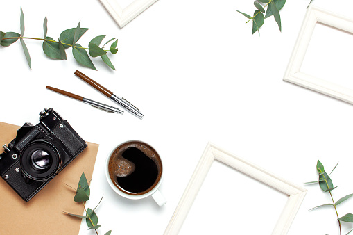 Photo frame old retro camera notebook diary cup of coffee pens eucalyptus leaves on white background. Flat lay top view copy space. Stylish minimal composition artwork mockup Feminine desk workspace.
