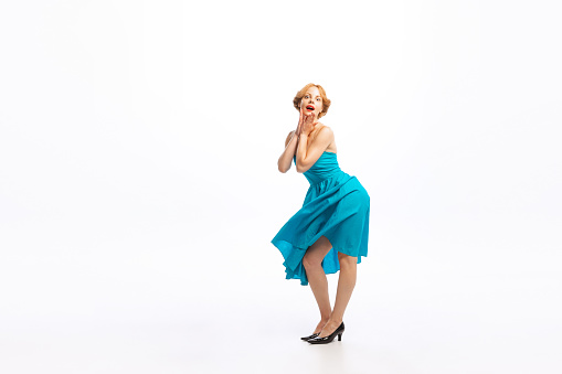 Portrait of beautiful young woman with blonde hair dancing in stylish retro dress isolated over white background. Concept of retro fashion, style, youth culture, emotions, beauty. Copy space for ad