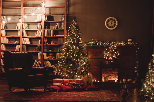 Christmas Interior. Hall in Christmas Lights. Christmas Tree, Fireplace and Library. Red New Year's interior. Evening Cozy Evening on Eve of Holiday.