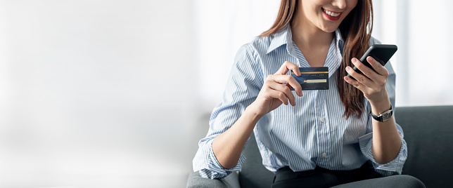 Young beautiful asian woman using credit card purchasing online via smartphone at home.