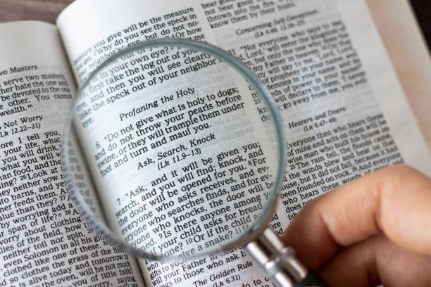 istock Ask, search, knock, biblical text verse, human hand holding a magnifying glass over Holy Bible Book 1411614404