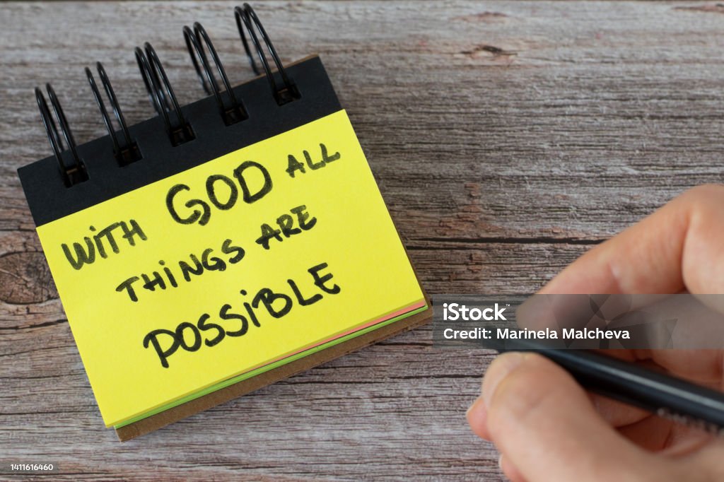 With God all things are possible, handwritten text on a yellow note with a hand on a wooden table With God all things are possible, handwritten text on a yellow note with a hand on a wooden table. Top view. A closeup. Miracle Stock Photo