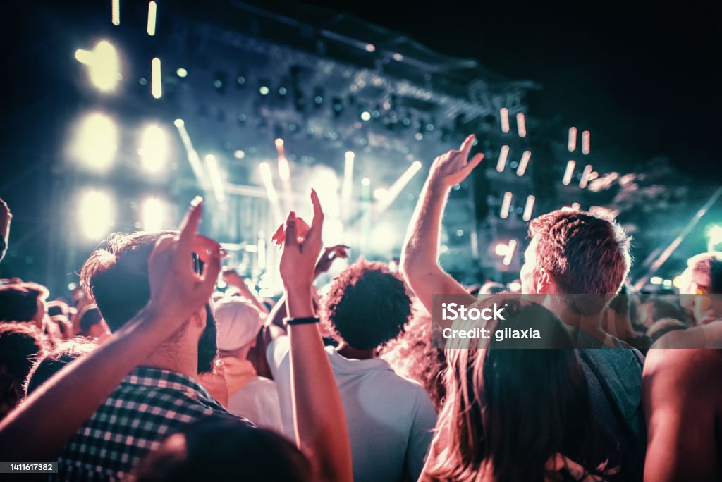 Rave party. Rear view of large group of people enjoying a concert performance.  People in foreground are released. Music Festival Stock Photo