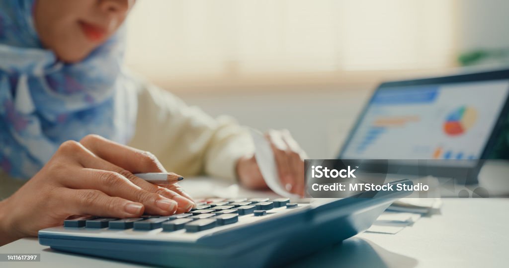 Closeup Asian muslim woman with hijab using tablet calculator focus on utility bills calculate check credit card receipt monthly expense bill in living room at house. Closeup Asian muslim woman with hijab using tablet calculator focus on utility bills calculate check credit card receipt monthly expense bill in living room at house. Home financial lifestyle concept. Investment Stock Photo