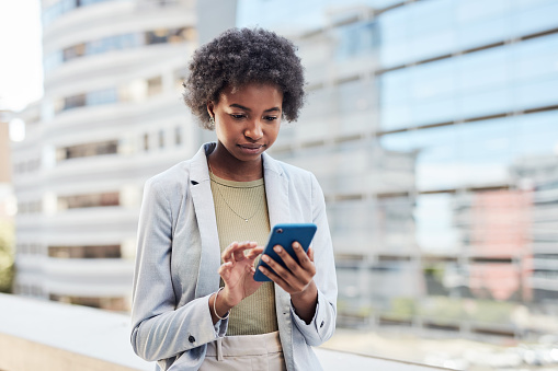 African american businesswoman using a phone while working in the city. An entrepreneur browsing social media and answering work emails while walking in town with a building exterior in the background
