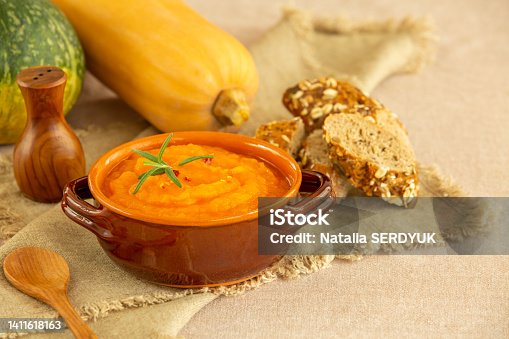istock Pumpkin and carrot soup in clay bowls and organic pumpkins with black bread on a linen background. Vegetarian autumn cream soup of pumpkin with seeds. Traditional autumn and winter food 1411618163