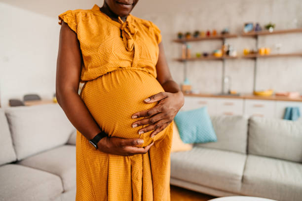 mujer negra disfrutando del embarazo en casa - holding belly fotografías e imágenes de stock