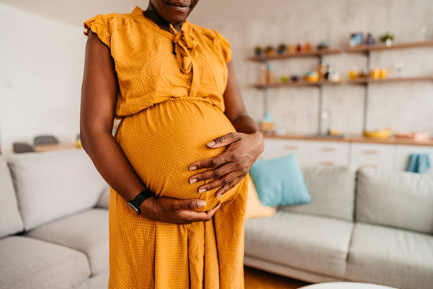 femme noire profitant de la grossesse à la maison - holding belly photos et images de collection