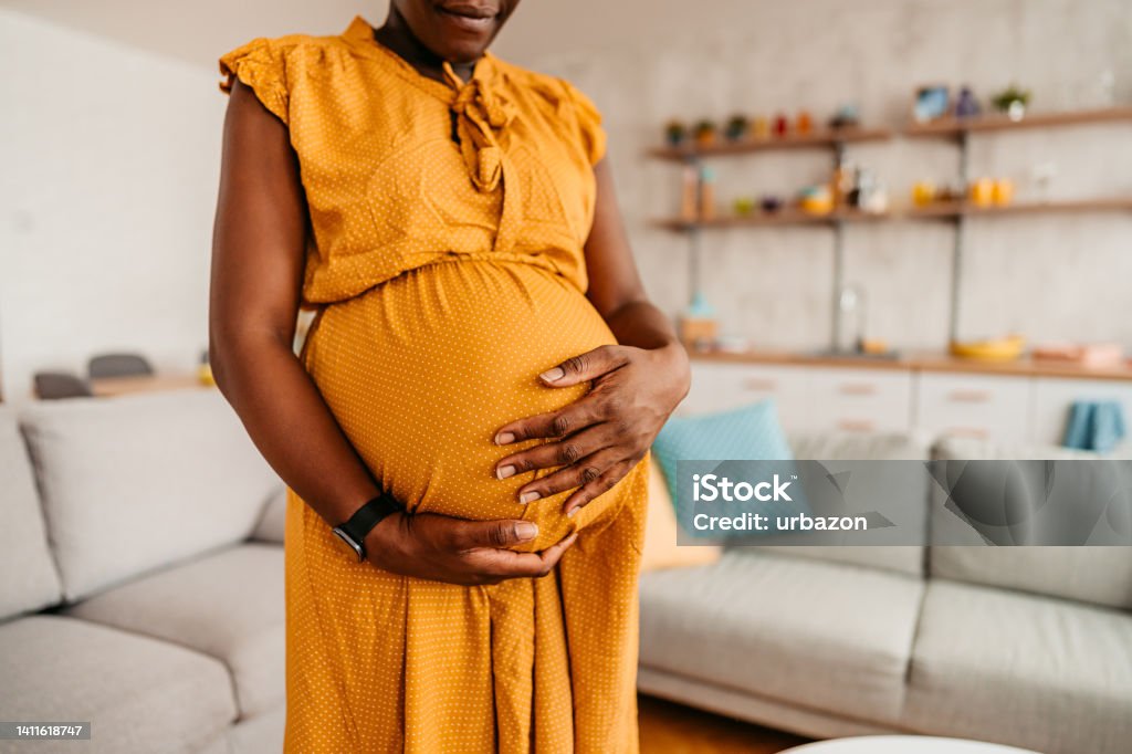 Black Woman Enjoying Pregnancy At Home Portrait of beautiful pregnant black mother holding her pregnant belly at home. Close-up. Pregnant Stock Photo
