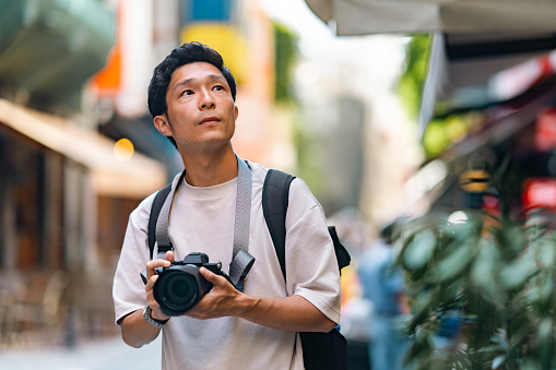 A young male tourist is taking photos with a camera in the streets of a historical town during his travel.