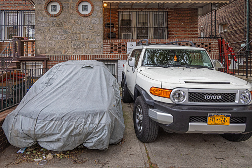 Tow cars in a driveway, one is a pickup truck and one is hidden under a tarpaulin, the picture is taken in Crescent Street in Long Island City, Queens