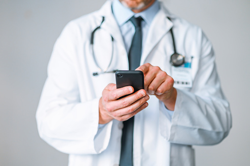 A doctor is texting using his phone sending a message to a person. Closeup of a healthcare professional searching the internet for information. A male GP scrolling or browsing the web