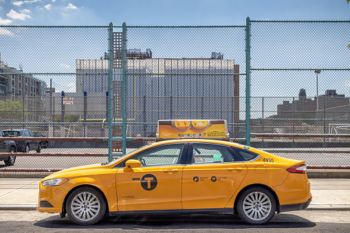 Yellow taxi in front of a wire fence in 12th Street in Long Island City which is a part of Queens and is a mixture of new and old, small industries and residential areas close to Manhattan, New York