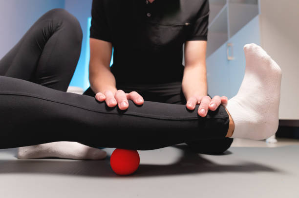 libération myofasciale. un physiothérapeute masculin met une balle pour réhabiliter les muscles des jambes d’un client assis à l’aide d’une balle rouge. le concept d’auto-massage. utilisation pratique. - technique photographique photos et images de collection