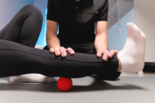 Myofascial release. A male physiotherapist puts a ball to rehabilitate the leg muscles of a client while sitting using a red ball. The concept of self-massage. Practical use