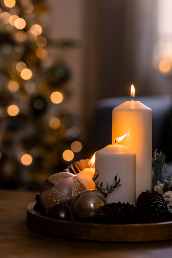 A close-up shot of Christmas decorations placed on a wooden table in a living room on a December day, candles are lit creating a warm feeling in the room.