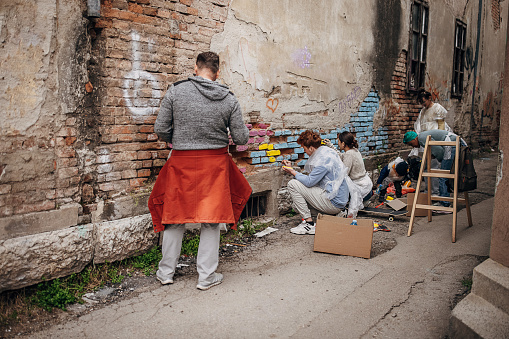 Group of male and female street artists drawing together on wall outdoors in city.