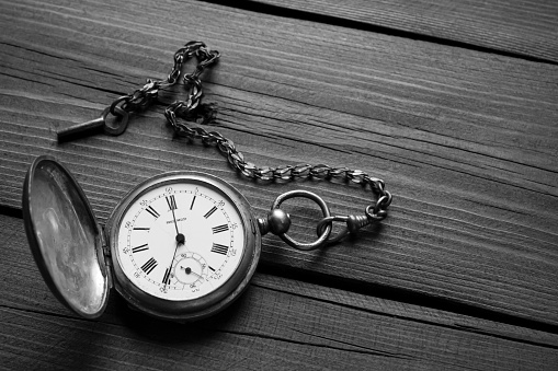 Black and white photo of silver, pocket watches. Clock - time on a wooden table. On the table are an open karman clock on a chain. Pocket watch made of silver on a chain. Open pocket watch.
