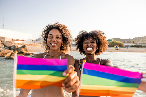 Two women standing for lgbtqia rights attending to a concert and parade on the beach in summertime.