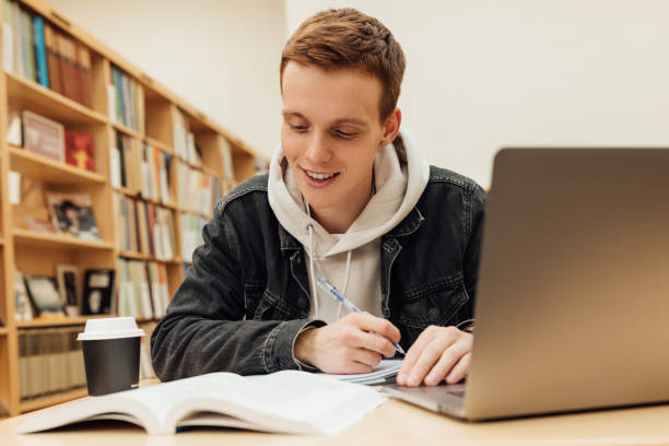 istock Smiling male student looking at notes while sitting at desk and preparing exams 1411632130