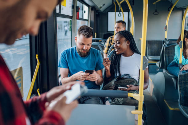 Multiracial friends talking and using a smartphone while riding a bus in the city stock photo