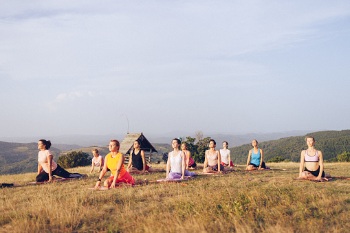Group of women doing yoga exercises on a hill , in non-urban area under open and clear skies.