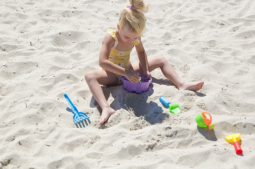 Cute happy 4 years old girl playing with plastic toys on the sandy beach.