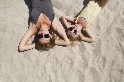 Happy little girl laying on the sand with her mother, top view. Happy idyllic family summer vacation concept.