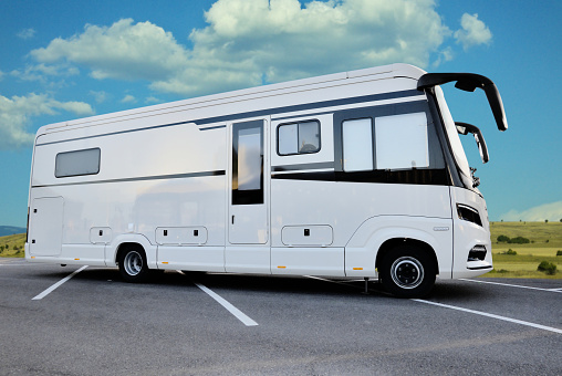 White camper bus parked on a parking lot near the field.