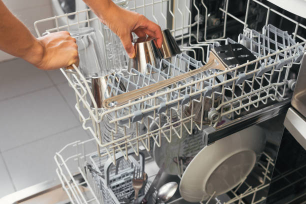 istock Woman's hands depositing or picking up a metal cup to make custard from the automatic dishwasher. Young girl placing the tray with glasses and plates to perform a wash with one of the appliances 1411650030