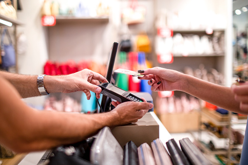 Close up on human hands during contactless payment with a credit card while salesman is holding a credit card reader and a female customer is paying after successful shopping of traveling bags.