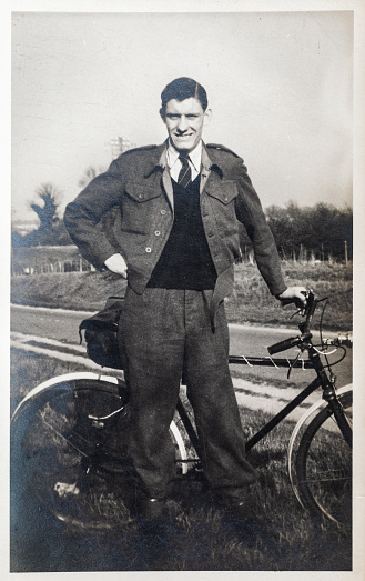 Young man out for a bike ride. Vintage photo of a teenager, approx aged 18, with push bike, standing at the side of a road. Black and white. Circa 1944.