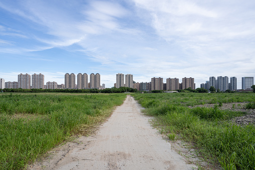 A dirt road on the grass leads to the city buildings in the distance
