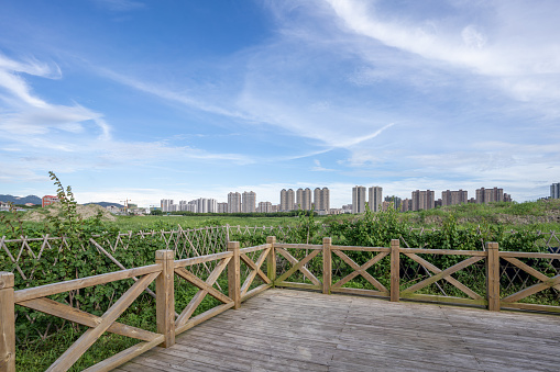 The guardrail of the wooden plank road in the Greenland Park and the city beside the grassland