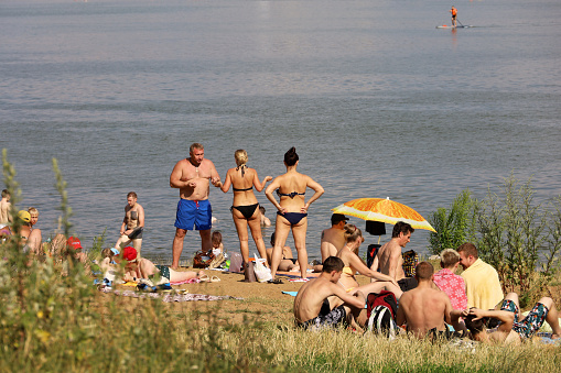 Moscow, Russia - July 2022: People sunbathing on a beach on background of Moscow river in Strogino district, women in bikini standing on a sand