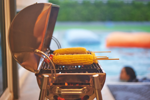 corn and barbecue sticks on stove on blur swimming pool background party