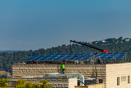 Installation of solar cell electric panels on a roof of multi-storey building in Israel. Solar panels on the house roof. Workers are installing the solar cell farm power plant. eco technology.