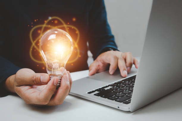 Hand man holding bulb light idea creativity inspiration and using computer laptop on desk. stock photo
